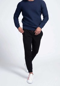 Maglione lavorato a maglia blu navy, pantaloni jogger neri con dettagli rossi e sneakers bianche con una striscia rossa. Texture lisce e design aderente.