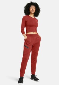 Červený športový crop top a zodpovedajúce jogger nohavice s užšími nohavicami, so sťahovacím pásom a zipsovým vreckom. Materiál vyzerá hladko a elasticky.