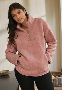 Lyserød fleece-pullover med halv-zip design, struktureret overflade og sidelommer, med en kontrastfarvet krave og manchetter.