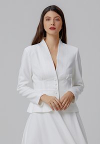 Blazer blanc ajusté avec un col châle, des manches longues et des boutons à l'avant. Tissu lisse avec un détail peplum structuré à la taille.