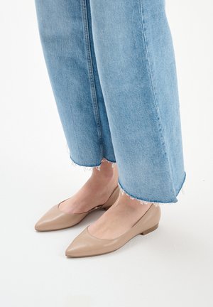 Beige leather flats with a pointed toe and low heel, worn with light blue frayed hem jeans. Smooth texture, minimal detailing.