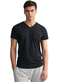 Camiseta negra de cuello en v hecha de algodón, diseño ajustado con mangas cortas, con un sutil logo en el pecho; combinada con pantalones grises con cordón.