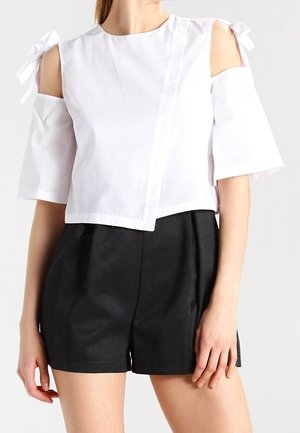 Haut blanc court avec design épaules dénudées, manches courtes et accents de nœud. Associé à un short noir taille haute. Texture lisse.