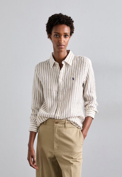 Striped long-sleeve shirt in beige and white with a subtle polo logo, paired with light beige pants, featuring a button-down collar and rolled sleeves.