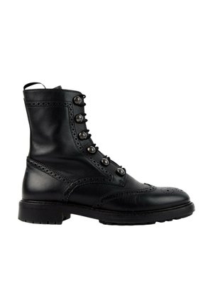 Zwarte leren enkelboot met brogue-details, zes metalen veteroogjes en een dikke rubberen zool, gezien van opzij.