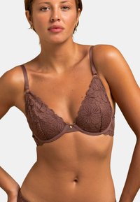 Soutien-gorge en dentelle marron avec motifs floraux, bonnets triangulaires, fines bretelles ajustables et un accent doré au centre. Texture de tissu lisse.