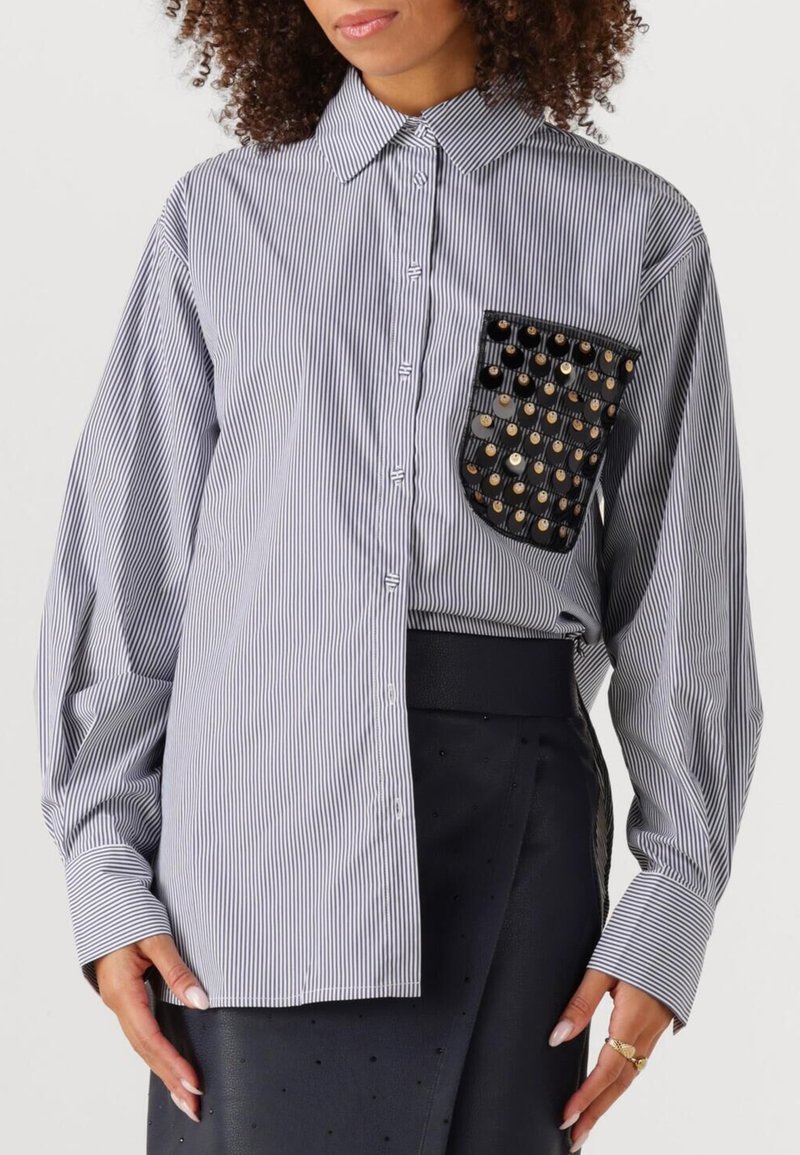 Gestreept overhemd in blauw en wit, met een zwarte borstzak versierd met metalen studs. Lange mouwen, met kraagontwerp.