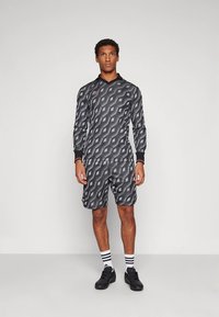 Conjunto deportivo en negro con patrones geométricos grises, camiseta de manga larga con cuello en V, pantalones cortos a juego, con detalles en negro y calcetines a rayas.