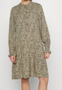 Abito a maniche lunghe con stampa zebrina beige e verde oliva, caratterizzato da un collo rotondo, dettagli con bottoni e una gonna a strati.