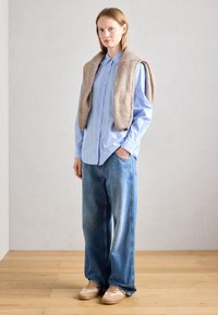 Chemise bleu clair à manches longues avec des rayures verticales ; pull sans manches beige et moelleux ; jean bleu clair décontracté ; baskets beiges.