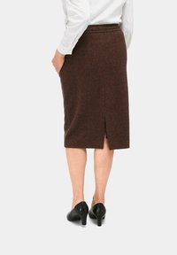 Jupe en chevrons marron au design longueur genou, avec une fente arrière et une taille élastique, associée à des chaussures à talons hauts noires.