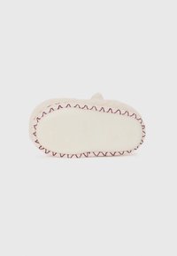 Chausson de couleur crème avec une texture douce, présentant une bordure en fil rouge contrastant et une semelle en caoutchouc antidérapante à motifs.