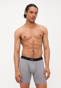 Šedé pánske boxerky s čiernym pásom, na ktorom je diskrétne logo. Tkanina sa zdá byť hladká a elastická, tesne priliehajúca k telu.