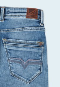 Světle modré džínové kalhoty s hnědou koženou značkovou nášivkou, jedinečným dvojitým stehem na zadním kapsu a opraným vzhledem.