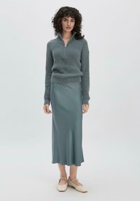 Pull en tricot bleu clair avec un col montant zippé, assorti à une jupe midi en satin bleu clair lisse et des ballerines crème.