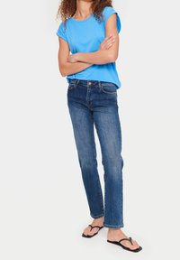 Blå kortärmad topp med rundad halsringning och lätt textur, tillsammans med mörk denim raka jeans och svarta flip-flops.