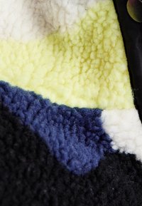 Farverigt fleece stof med et struktureret mønster i sort, blå, gul og hvid. Blødt, plysset tekstur med tydelige farveblokke.