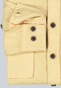 Khakifarbenes Hemd mit gefaltetem Design, dunklen Knöpfen, zwei Fronttaschen und einem orangefarbenen Akzent, der aus einer Tasche herausblitzt. Glatte Stofftextur.