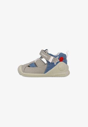 Zapato infantil gris y azul con suela de goma, parte superior de tela, detalles de estrella y sonrisa, y correa de Velcro para ajuste.