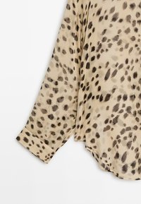 Beige long sleeve shirt with black and dark brown irregular leopard spots and a buttoned cuff on a white background.