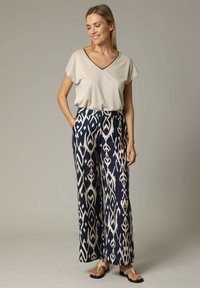 Haut beige à col en V avec des manches courtes, associé à un pantalon navy à jambes larges ornés d'un motif ikat crème. Les chaussures comprennent des sandales plates.