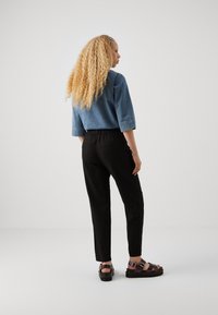 Džínová bunda s 3/4 rukávy, černé elastické kalhoty a sandály na pásky. Vlastnosti: kudrnaté blond vlasy a neutrální pozadí.