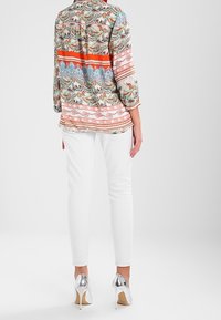 Long-sleeve patterned blouse in various pastel colors. Paired with fitted white pants and shiny silver high heels. Soft fabric texture.