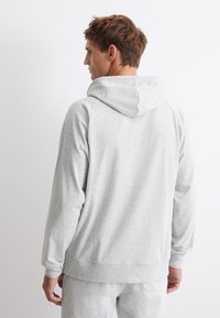 Ljust grå huvtröja med mjuk textur, avslappnad passform, raglanärmar och ribbade muddar. Baksidan har en enkel, unoberoende design.