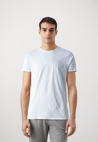 T-shirt en coton bleu clair avec un col rond, des manches courtes et une texture lisse. Porté avec un pantalon de survêtement gris, au design minimaliste.