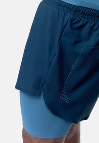 Pantaloni da allenamento blu navy con un elastico in vita e una tasca in rete. Sotto, pantaloncini attillati azzurri chiari con tessuto testurizzato.