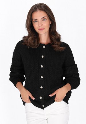 Zwarte kabelgebreide cardigan met een ronde halslijn, voorzien van een rij zilveren knopen en geribde manchetten. De stof lijkt textuur en warmte te hebben.