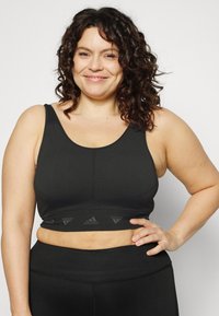 Top desportivo preto com textura canelada e alças largas, apresentando uma faixa elástica na parte inferior com o logo da Adidas.