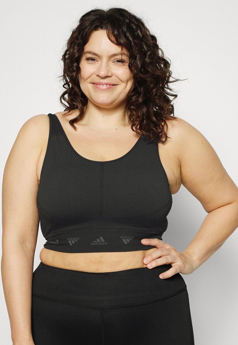 Top desportivo preto com textura canelada e alças largas, apresentando uma faixa elástica na parte inferior com o logo da Adidas.