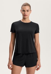 Top nero a maniche corte con scollatura rotonda, texture liscia e vestibilità ampia. Abbinato a pantaloni corti neri coordinati, anch'essi dal design rilassato.