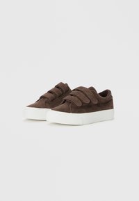 Brown corduroy sneakers with white rubber soles and three hook-and-loop straps on the upper. Features a textured fabric finish.