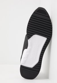 Mustan urheilukengän pohja, jossa on teksturoitu kumi pitoa varten, valkoisella välikannella ja kohopainetulla Puma-logolla. Siistit linjat ja moderni muotoilu.