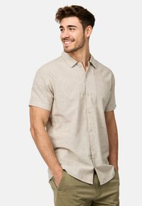 Camisa beige de manga corta con cuello, tejido texturizado y cierre de botones en el frente. Combinada con pantalones verde olivo.