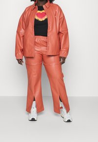 Coral faux leather jacket and pants set with a cropped black T-shirt featuring a colorful heart design. Pants have side splits and snap details.