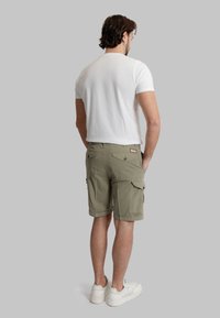 Maglietta bianca a maniche corte con scollo rotondo, abbinata a pantaloni cargo oliva con più tasche e orlo arrotolato. Scarpe da ginnastica bianche completano il look.