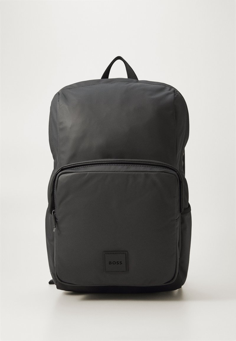 Sac à dos en nylon noir avec une surface texturée, doté d'une poche frontale zippée et d'une poignée rembourrée sur le dessus. Patch avec le logo à l'avant.