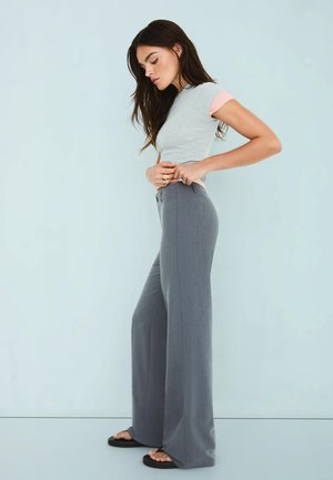 Pantaloni largi gri cu talie înaltă, dintr-un material croit, cu o textură netedă. Asociați cu un top gri deschis, cu mâneci roz.