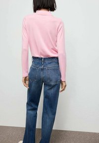 Rosa langärmliges Polohemd mit Kragen, kombiniert mit hochgeschnittenen blauen Jeans im Schlagstil, die über hintere Taschen und eine strukturierte Oberfläche verfügen.