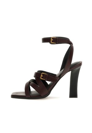 Dunkelbraune Leder-Hochsandale mit gekreuzten Riemen, zwei goldenen Schnallen, quadratischer Zehenpartie und dickem Absatz.