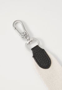 Sangle en cuir et toile avec un clip en métal argenté, présentant un accent en cuir noir et une surface texturée, principalement dans des couleurs beige et noir.