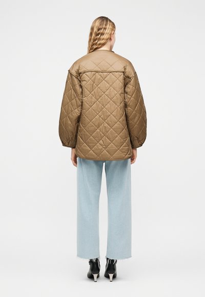 Άτομο με μακριά ξανθά μαλλιά που φοράει καφέ καπιτονέ μπουφάν, ανοιχτό μπλε παντελόνι φαρδιάς γραμμής και μαύρα μποτάκια με τακούνι, στραμμένο προς τα πίσω.