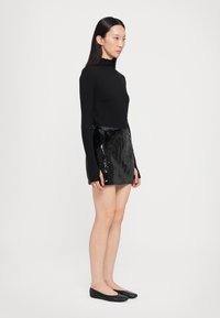 Top lung cu mânecă lungă neagră și fustă mini strălucitoare neagră cu paiete. Fusta are o textură cu model. Pantofii plat neagră completează ținuta.