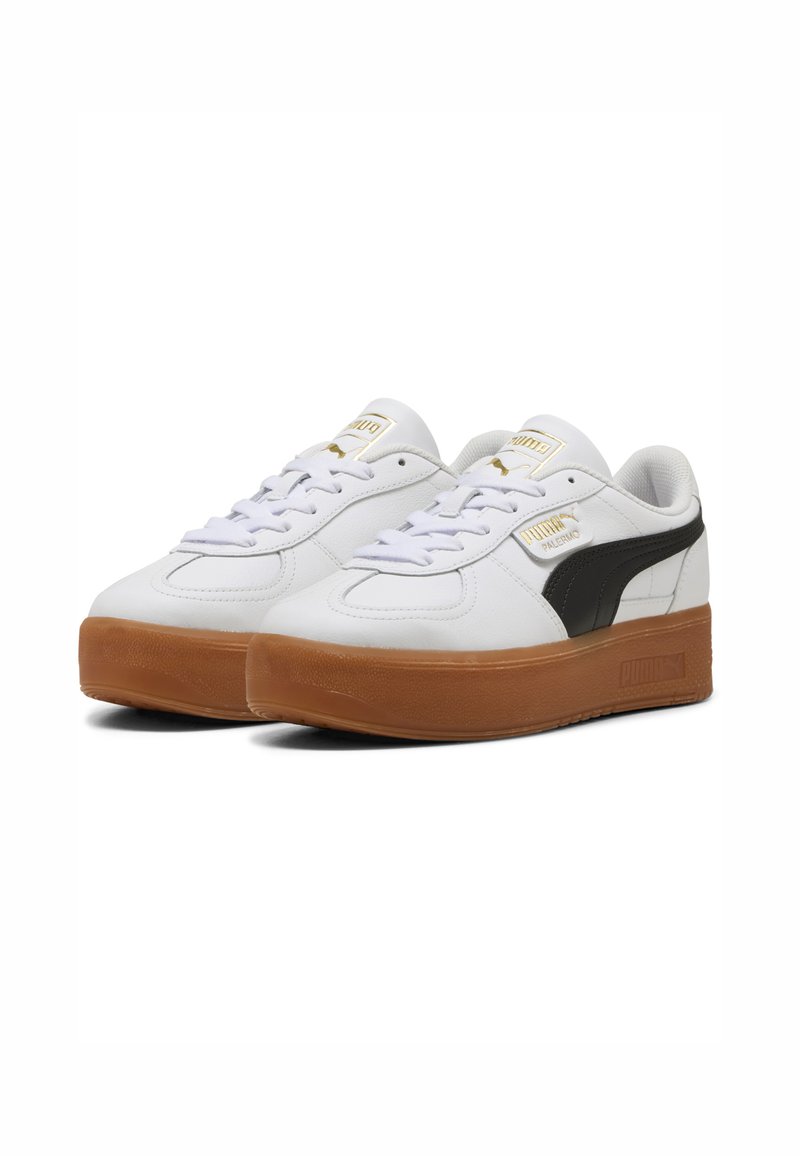 Białe sneakersy z gładką skórzaną cholewką, czarnym paskiem po boku, złotymi logo i grubą gumową podeszwą. Posiadają sznurowany krój oraz wyściełany język.