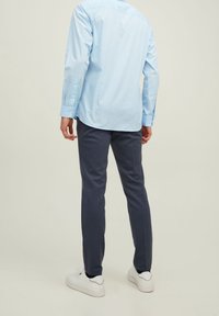 Light blue long-sleeve shirt with a button-down collar, paired with dark gray slim-fit pants and white sneakers, shown from the back.
