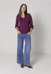 Bordeauxfarbenes V-Ausschnitt-Sweatshirt mit aufgerollten Ärmeln, kombiniert mit hellblauen weiten Jeans und braunen Absatzstiefeletten. Einfache, legere Kleidung.