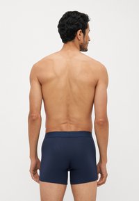 Mørkeblå bomullsboxershorts med myk elastisk midje, med en tettsittende design og lengde til midten av låret, vist bakfra.